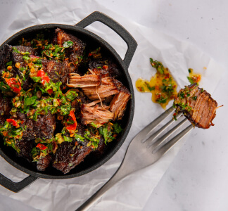 Bar and Block starter of burnt ends in green chimichurri sauce in a metal dish with a fork.