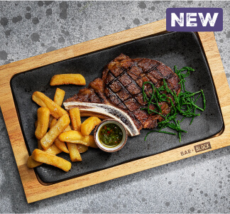 Bar and Block Côte de Boeuf steak with chips and a pot of green chimichurri served on a wooden platter.