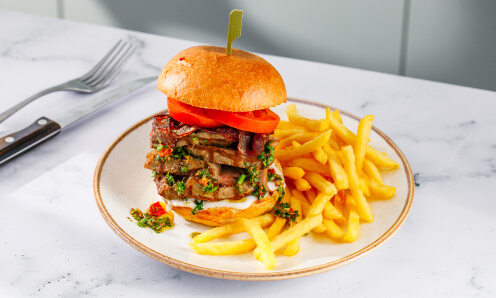 Bar and Block sirloin steak burger stacked with green chimichurri sauce and tomatoes in a brioche bun with chips.