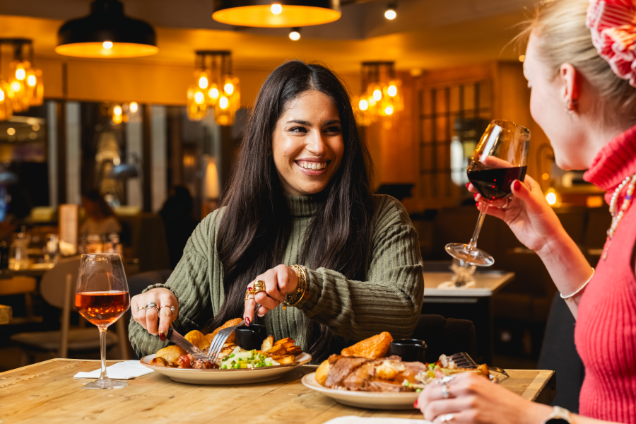 Two friends toasting and drinking red wine over a Bar and Block Sunday roast.